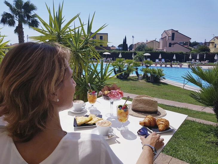 Frau genießt Frühstück mit Poolblick im Freien.