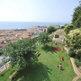 Grüner Garten mit Spielplatz, Bänken, Bäumen und Blick auf die Stadt und das Meer.