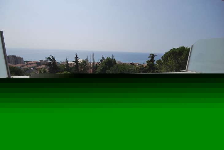 Balkon mit weißem Tisch und Stühlen, Blick aufs Meer und Bäume im Hintergrund.