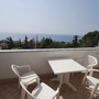 Balkon mit weißem Tisch und Stühlen, Blick aufs Meer und Bäume im Hintergrund.