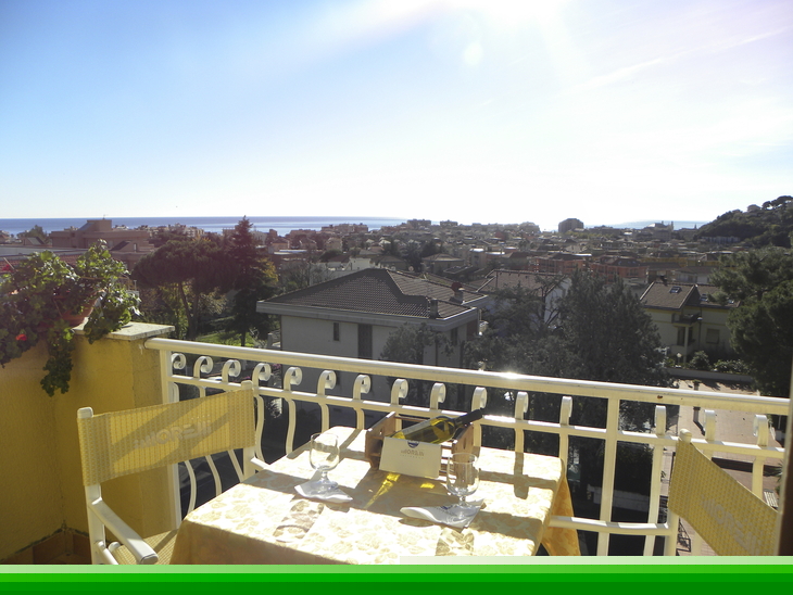 Blick von einem Balkon auf ein Dorf und das Meer im Hintergrund bei sonnigem Wetter.