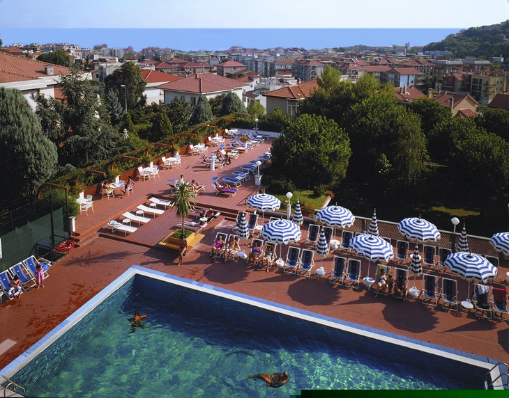 Blick auf ein Freibad mit Liegen, Sonnenschirmen und angrenzender Stadt im Hintergrund.