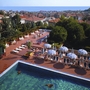 Blick auf ein Freibad mit Liegen, Sonnenschirmen und angrenzender Stadt im Hintergrund.