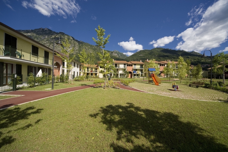 Wohnanlage mit Garten, Spielplatz und Bergen im Hintergrund.