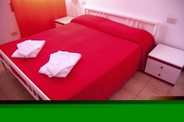 Rotes Doppelbett mit weißen Handtüchern in einem Schlafzimmer.