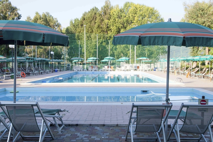 Schwimmbad mit Liegestühlen und Sonnenschirmen in einer Ferienanlage.