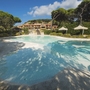 Pool im Roccamare Resort umgeben von Bäumen und Sonnenschirmen.