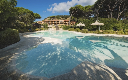 Pool im Roccamare Resort umgeben von Bäumen und Sonnenschirmen.