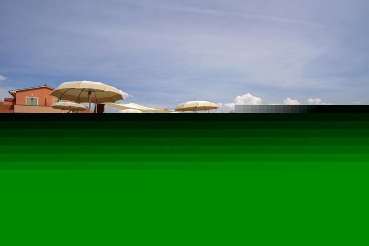 Strandliegen und Sonnenschirme auf einem Sandstrand vor Gebäuden.