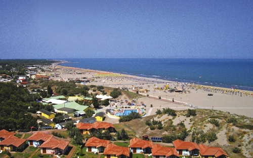 Luftaufnahme eines Küstenbereichs mit Strand und Gebäuden im Hintergrund.