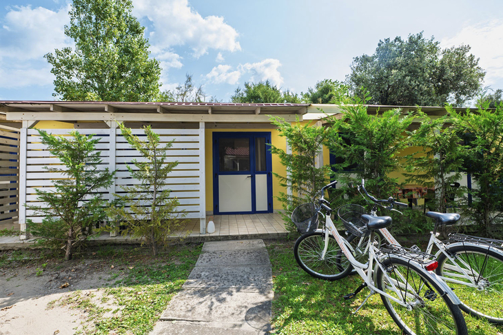 Ein Doppelbungalow mit Fahrrädern davor, umgeben von Bäumen und Sträuchern.