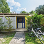 Ein Doppelbungalow mit Fahrrädern davor, umgeben von Bäumen und Sträuchern.