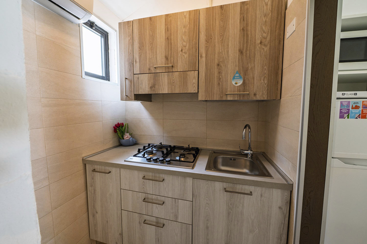 Kleine Küche mit Holzschränken, Gasherd, Spüle und Wandfenster.