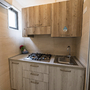 Kleine Küche mit Holzschränken, Gasherd, Spüle und Wandfenster.