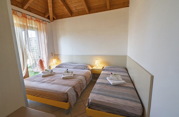Zwei Einzelbetten in einem hellen Zimmer mit Holzdecke und Nachtlichtern.