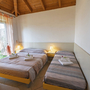 Zwei Einzelbetten in einem hellen Zimmer mit Holzdecke und Nachtlichtern.