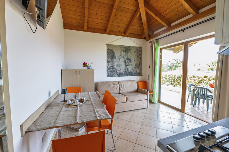 Helles Wohnzimmer mit Tisch, orangefarbenen Stühlen, Sofa und großer Glastür zur Terrasse.