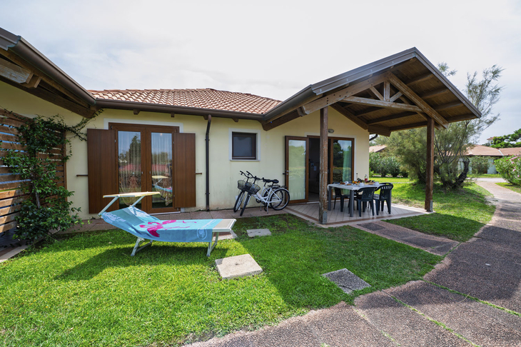 Ferienhaus mit Terrasse, Liegestuhl und Fahrrädern auf einer grünen Wiese.