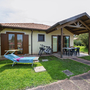 Ferienhaus mit Terrasse, Liegestuhl und Fahrrädern auf einer grünen Wiese.
