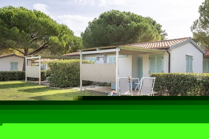 Bungalow mit Veranda und Gartenstühlen unter Bäumen.