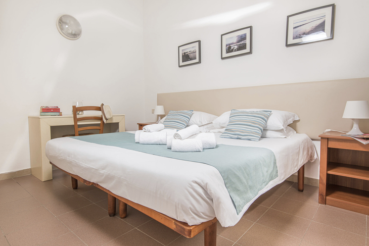 Doppelbett in einem hellen Bungalowzimmer mit zwei Nachttischen und Wandbildern.