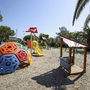 Spielplatz mit buntem Klettergerät und Rutsche unter Palmen.