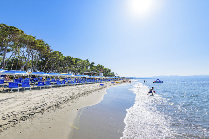 Strand von Piombino mit Liegestühlen und Sonnenschirmen, Person am Wasser, sonniger Himmel.