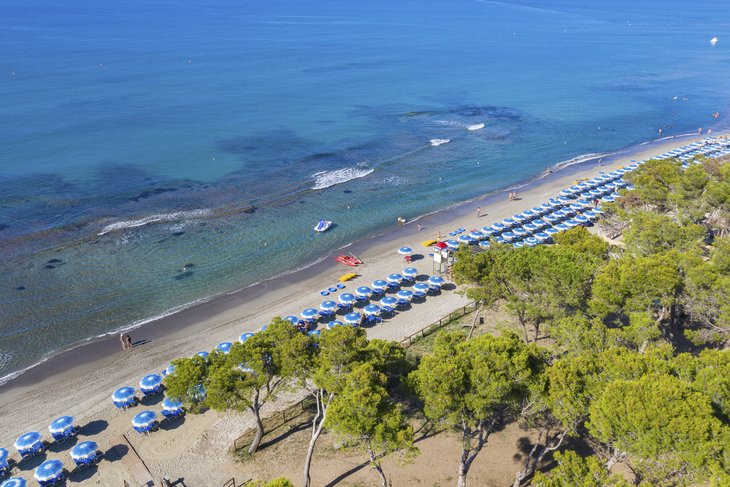 Luftaufnahme eines Strandes mit Sonnenschirmen und klarem, blauem Meer in Piombino.