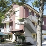 Drei-stöckiges Wohnhaus mit Treppe und Balkon, umgeben von Bäumen.