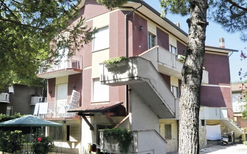 Drei-stöckiges Wohnhaus mit Treppe und Balkon, umgeben von Bäumen.