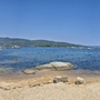 Panorama einer Bucht mit Sandstrand und klarem Wasser, umgeben von Bergen und Bäumen.
