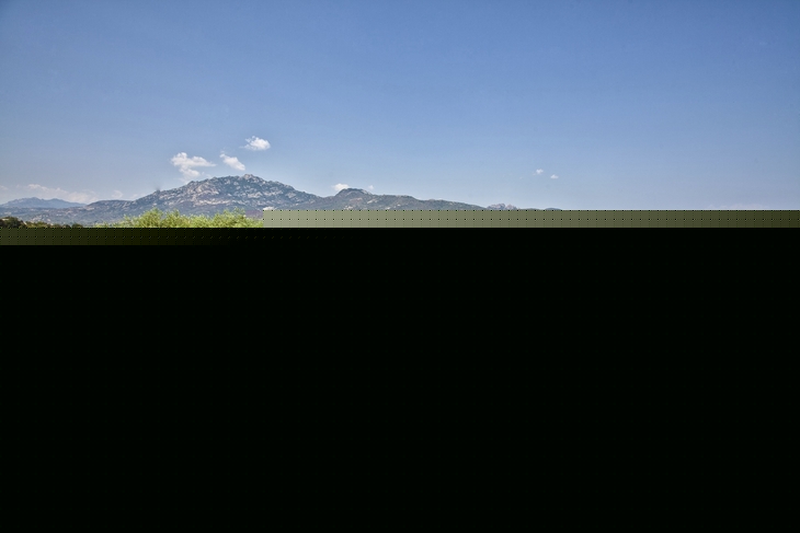 Garten mit Bäumen und einem Gebäude im Hintergrund, blaue Berge in der Ferne.
