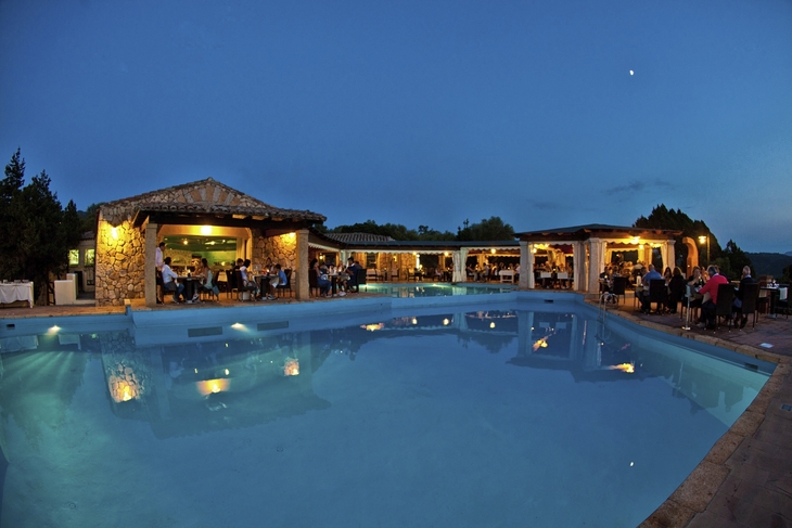 Nachtaufnahme eines beleuchteten Pools in Porto Rotondo mit Menschen im Hintergrund.