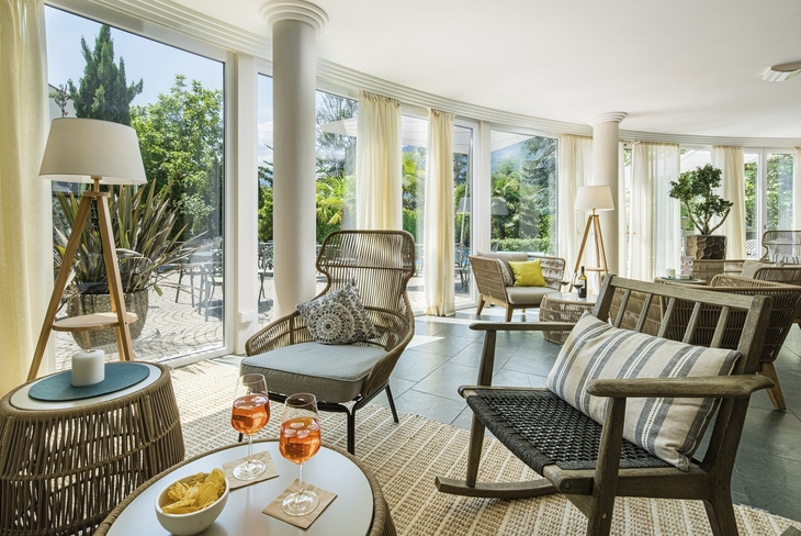 Helle Lounge mit Rattansesseln und großen Fenstern, Getränke auf Tisch.