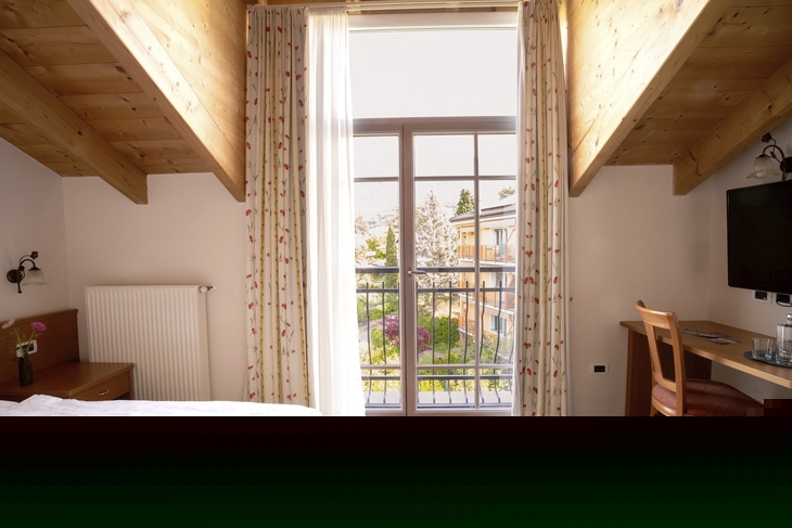 Helles Hotelzimmer mit Holzmöbeln und Balkonblick auf die Umgebung.