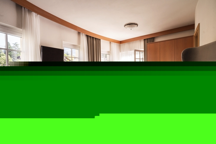 Helles Hotel-Doppelzimmer mit Doppelbett, Schreibtisch und großem Fenster.