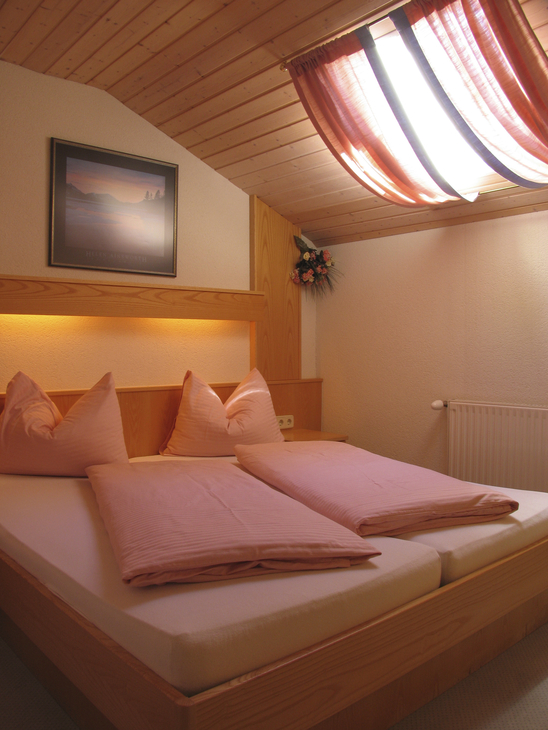 Doppelbett in gemütlichem Holz-Schlafzimmer mit Rotlichtbeleuchtung und Dachfenster.
