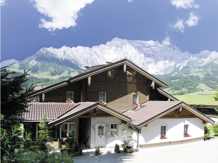 Ein Landhaus vor Alpenkulisse bei klarem Himmel.