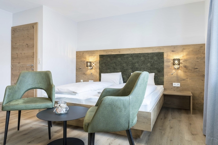 Modernes Apartment-Schlafzimmer mit Doppelbett, grünen Stühlen und Holzelementen.