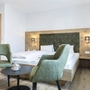 Modernes Apartment-Schlafzimmer mit Doppelbett, grünen Stühlen und Holzelementen.