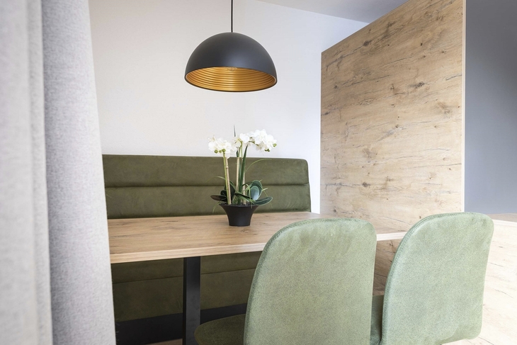 Essbereich mit Holztisch, grüner Sitzbank und modernen Stühlen in einem Studio