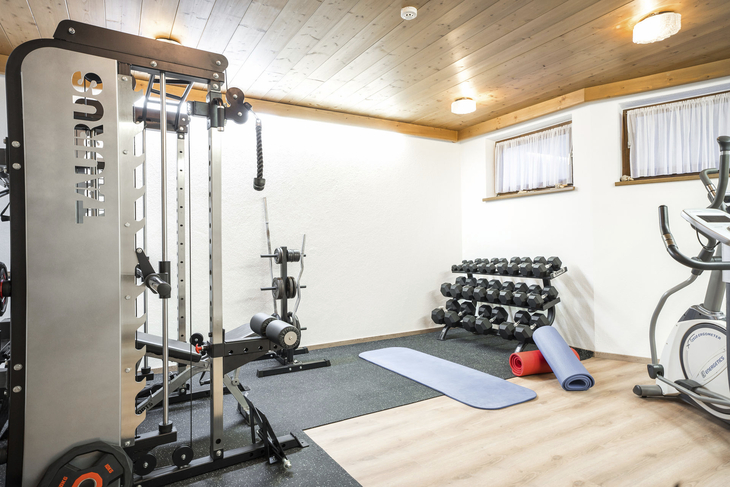 Fitnessraum mit Geräten, Hanteln und Yogamatten in einem hell erleuchteten Raum.