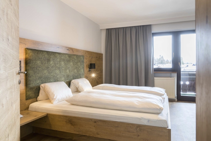 Doppelzimmer mit Holzinterieur und großem Fenster, Gardinen und Doppelbett.
