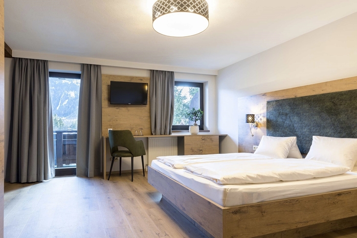 Modernes Schlafzimmer mit Doppelbett, Schreibtisch und Blick aus dem Fenster.