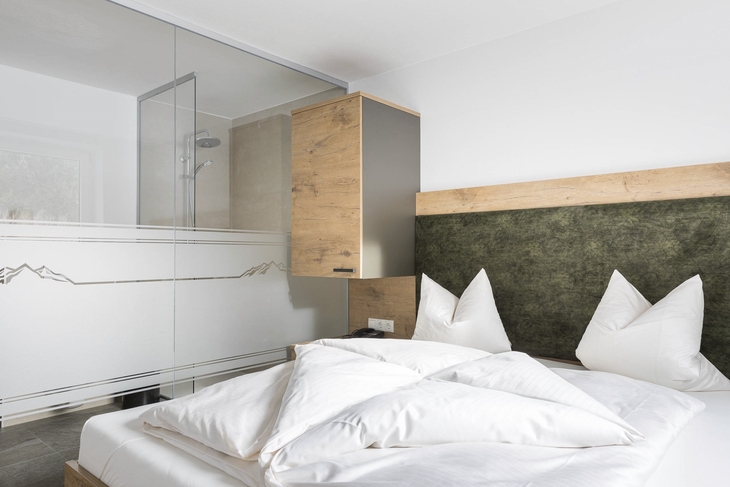 Modernes Hotelzimmer mit Doppelbett und Glasdusche im Hintergrund.