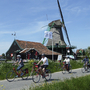Radfahrer auf einem Weg neben einer Windmühle in Nordholland bei sonnigem Wetter