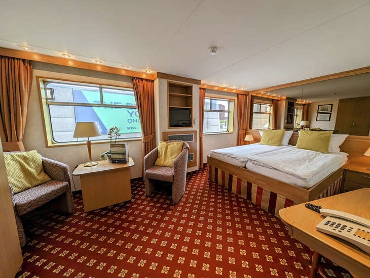 Junior Suite auf dem Oberdeck mit Doppelbett und Sitzbereich, stilvoll eingerichtet.