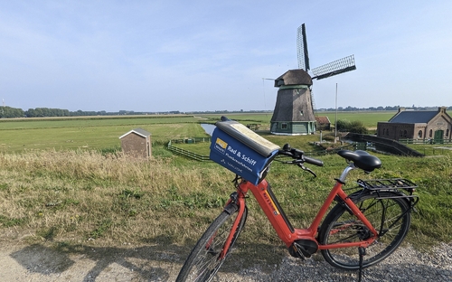 Rotes Fahrrad vor einer Windmühle in einer weiten, grünen Landschaft.