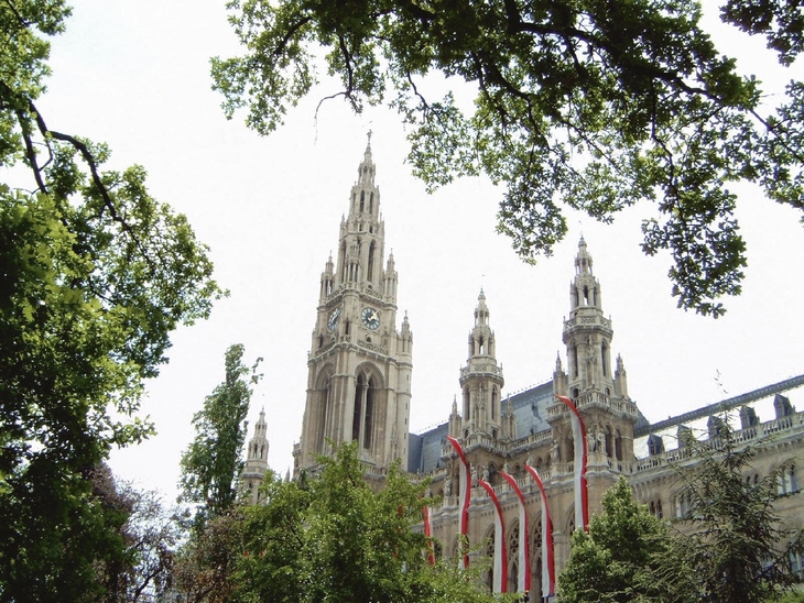 Wiener Rathaus, gotischer Stil, mit Bäumen im Vordergrund und österreichischen Fahnen.