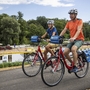 Zwei Personen fahren mit Fahrrädern auf einem Radweg entlang eines Flusses.
